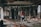 A person wearing a red shirt and shorts is standing in the middle of a destroyed building with exposed insulation and wooden supports. The surroundings are cluttered with debris, broken structures, and insulation material scattered on the floor.