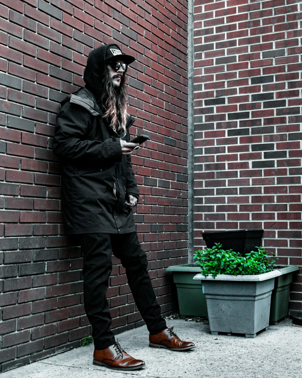 man in black leather jacket and black pants standing beside brown brick wall