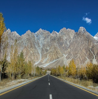 gray concrete road near trees and mountain under blue sky during daytime