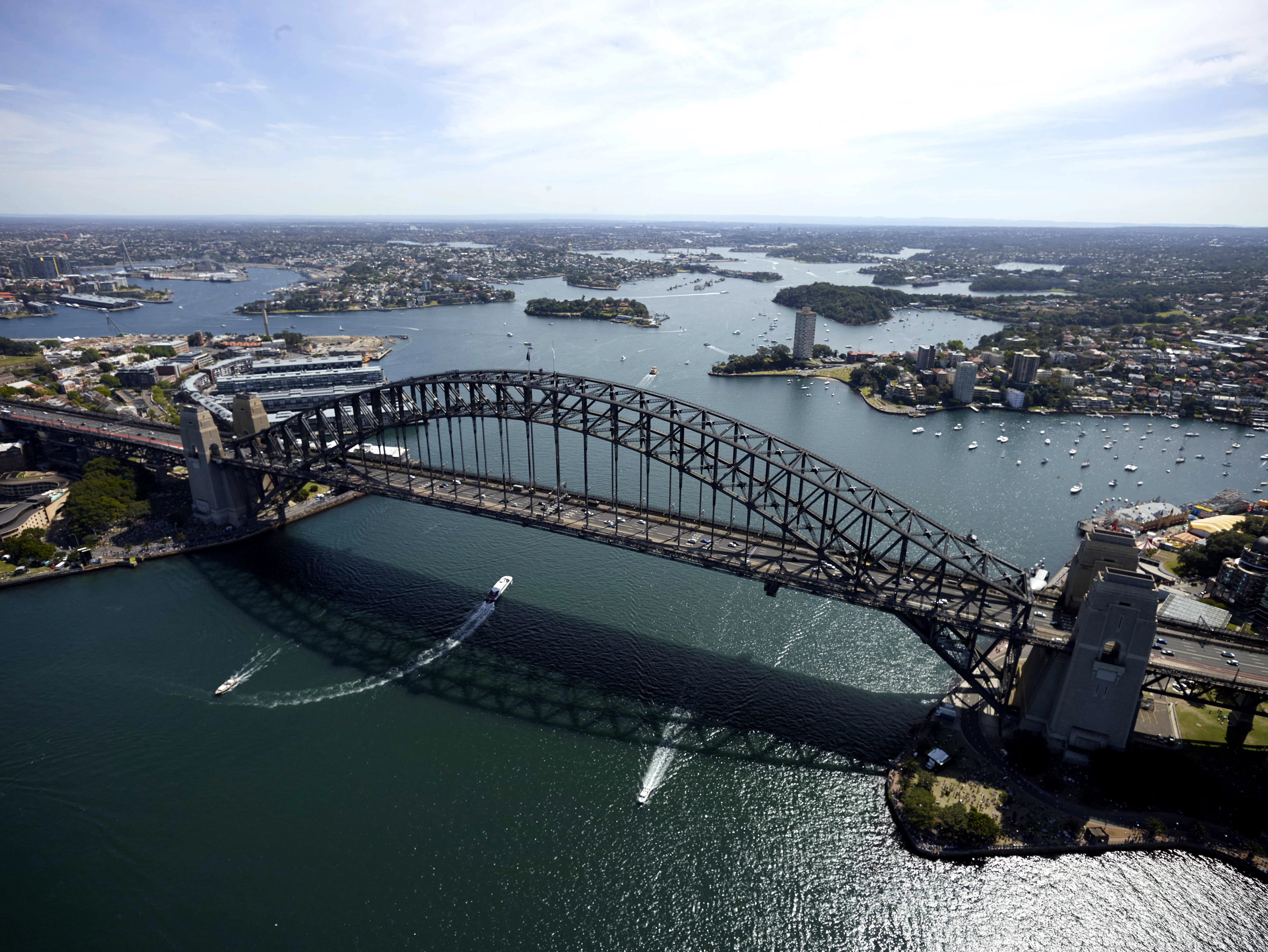 An aerial view of Sydney Harbour Bridge spanning the water, with boats and green islands beyond