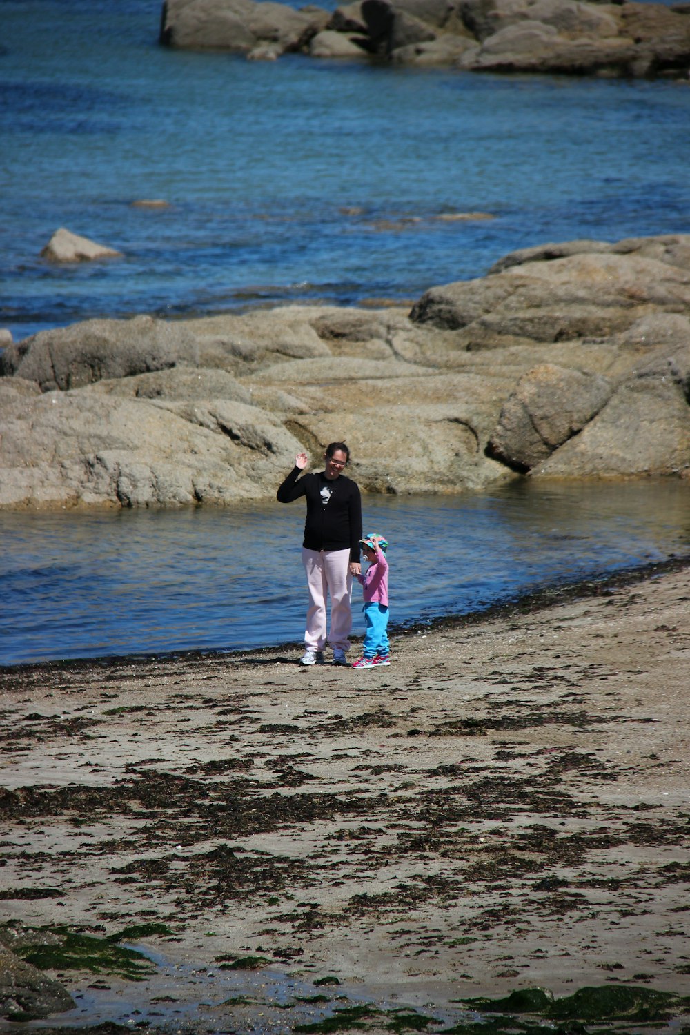 girl in black shirt and pink pants standing on brown rock near body of water during
