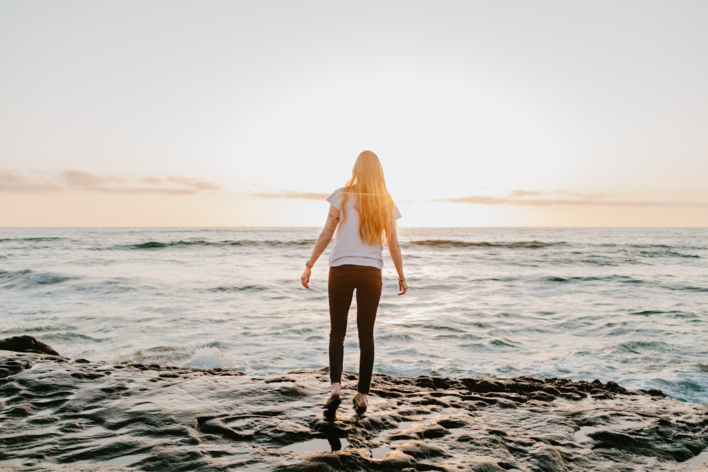 woman in white long sleeve shirt and black shorts standing on beach shore during daytime