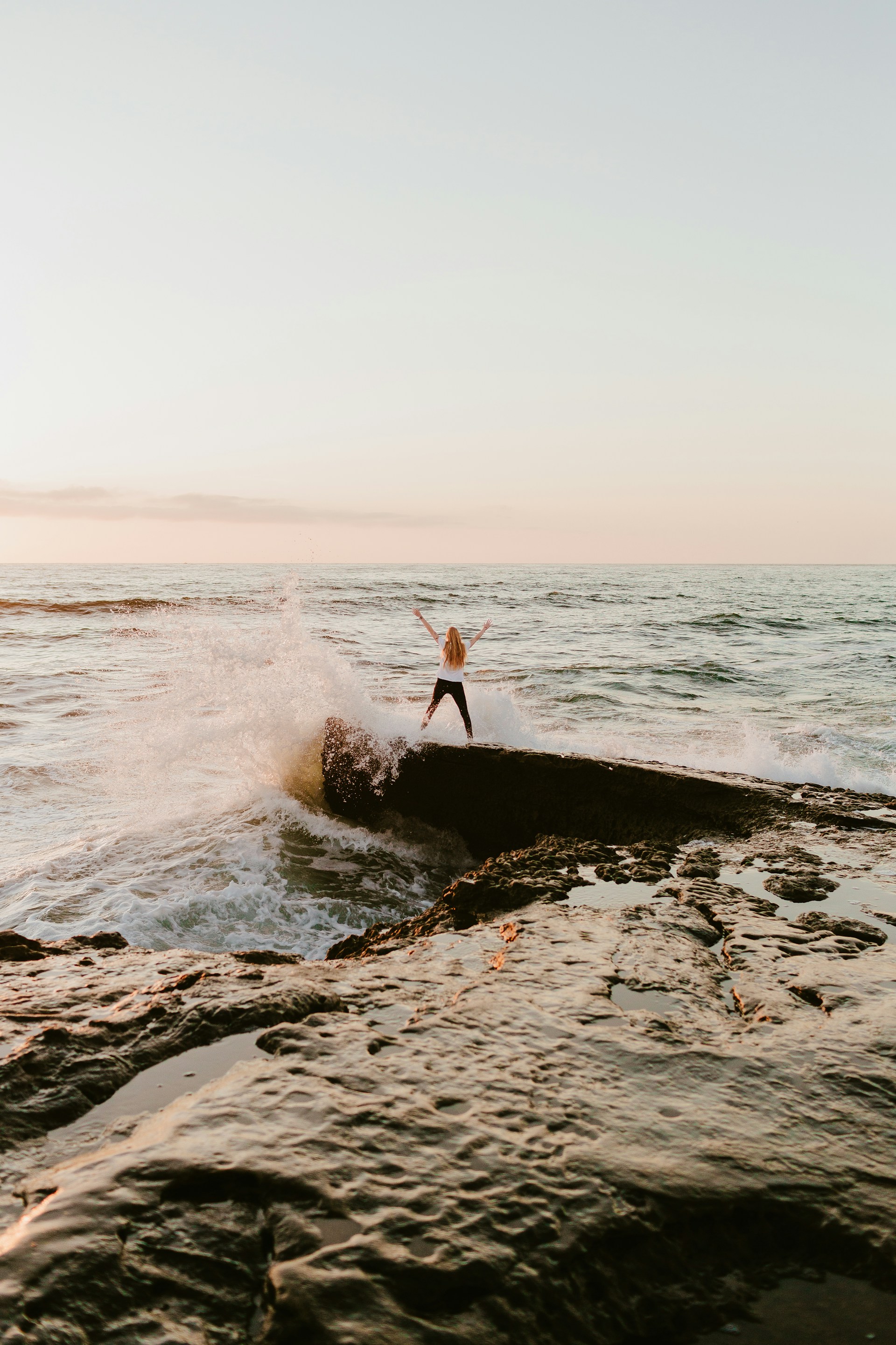 man in orange shirt standing on rock near sea during daytime