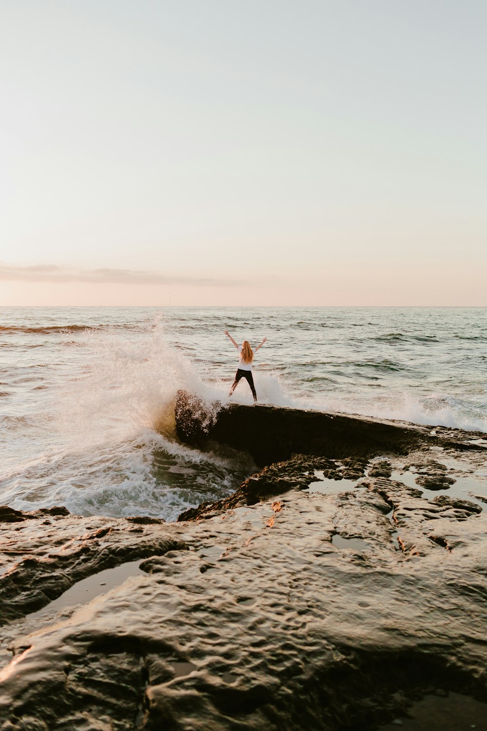 man in orange shirt standing on rock near sea during daytime