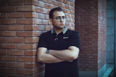 a man leaning against a brick wall with his arms crossed
