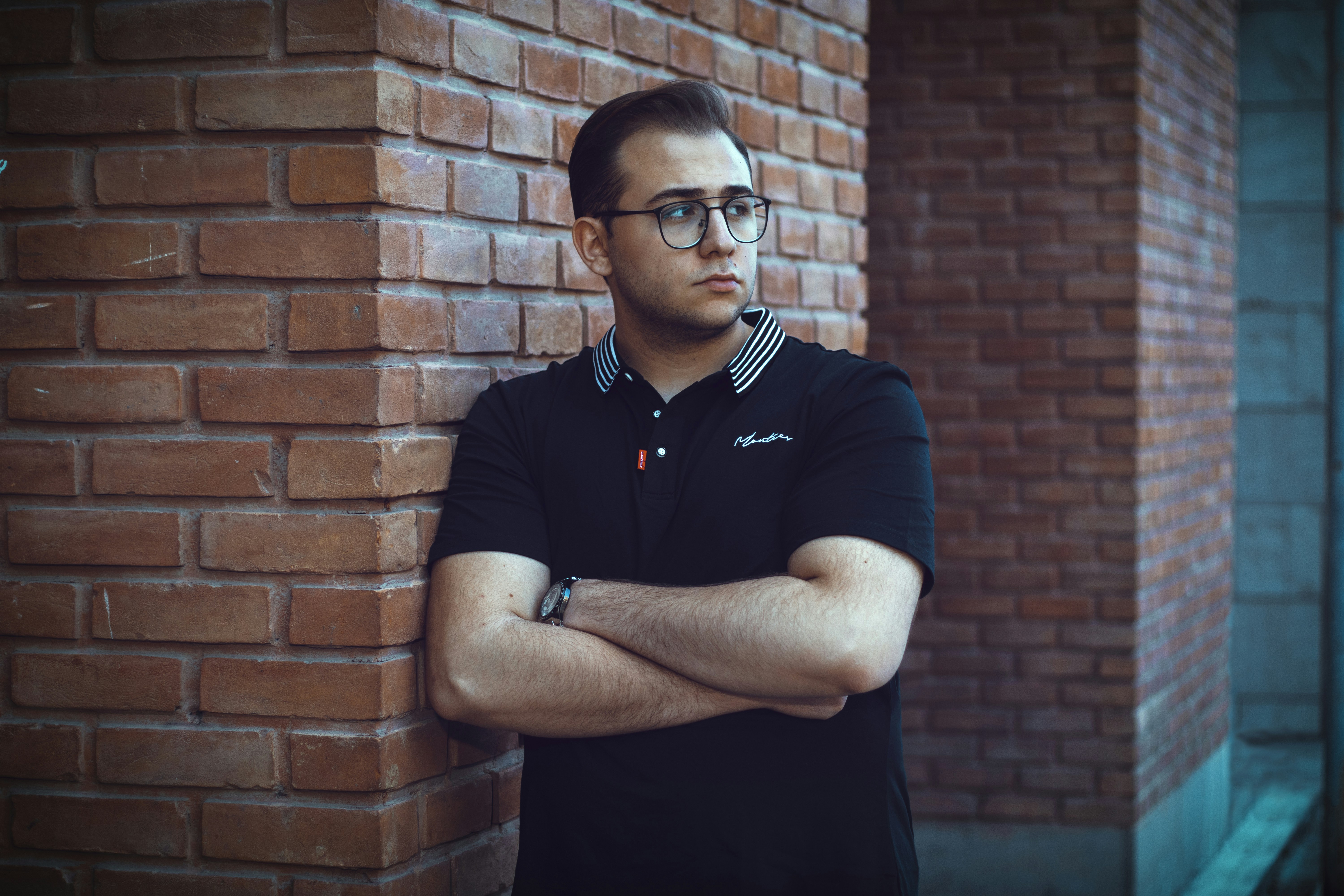 a man leaning against a brick wall with his arms crossed