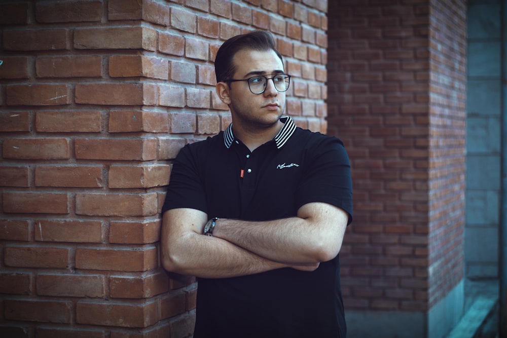 a man leaning against a brick wall with his arms crossed