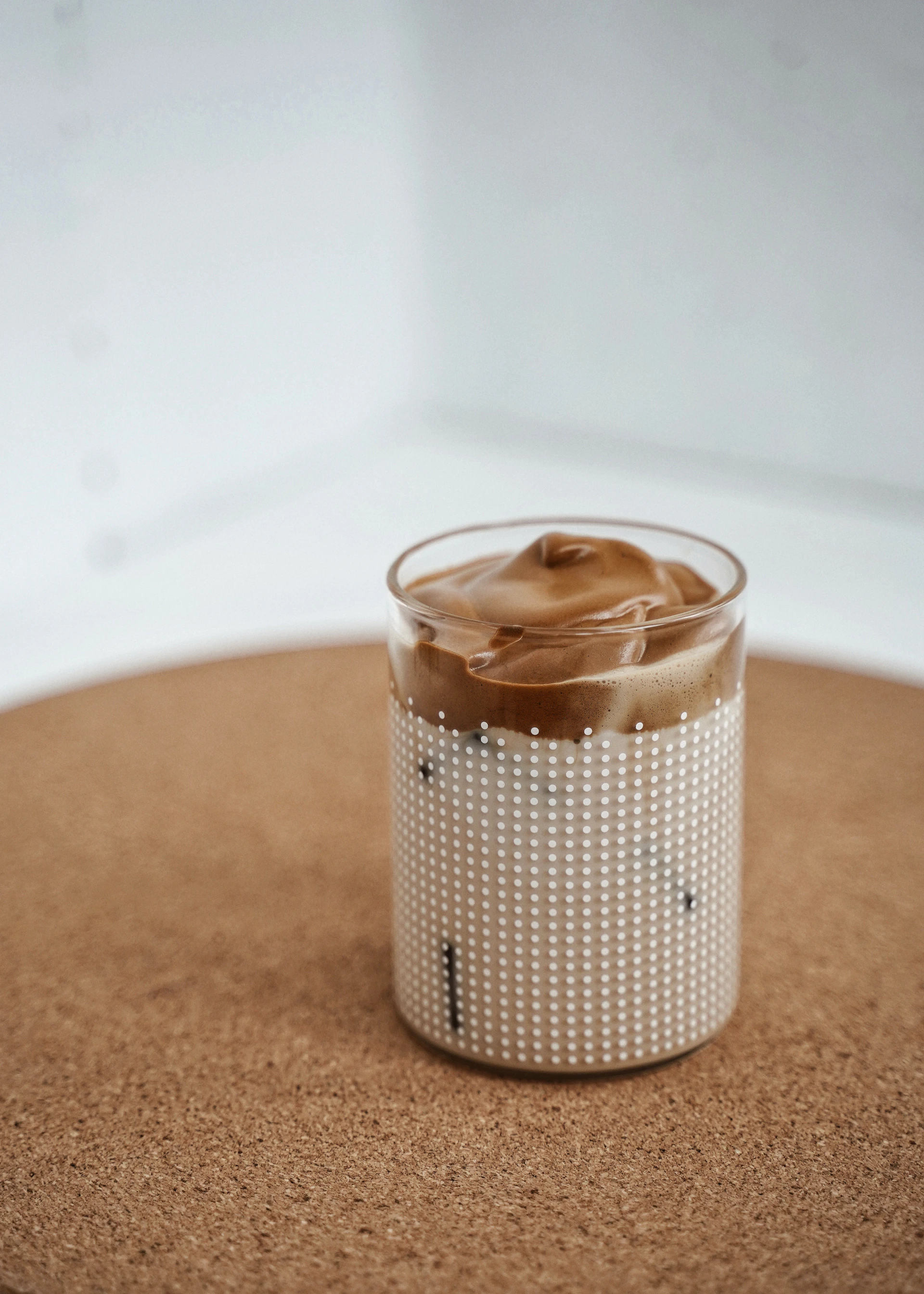 A bright, modern café-style layered coffee drink with creamy milk froth on top, set against a clean white background.