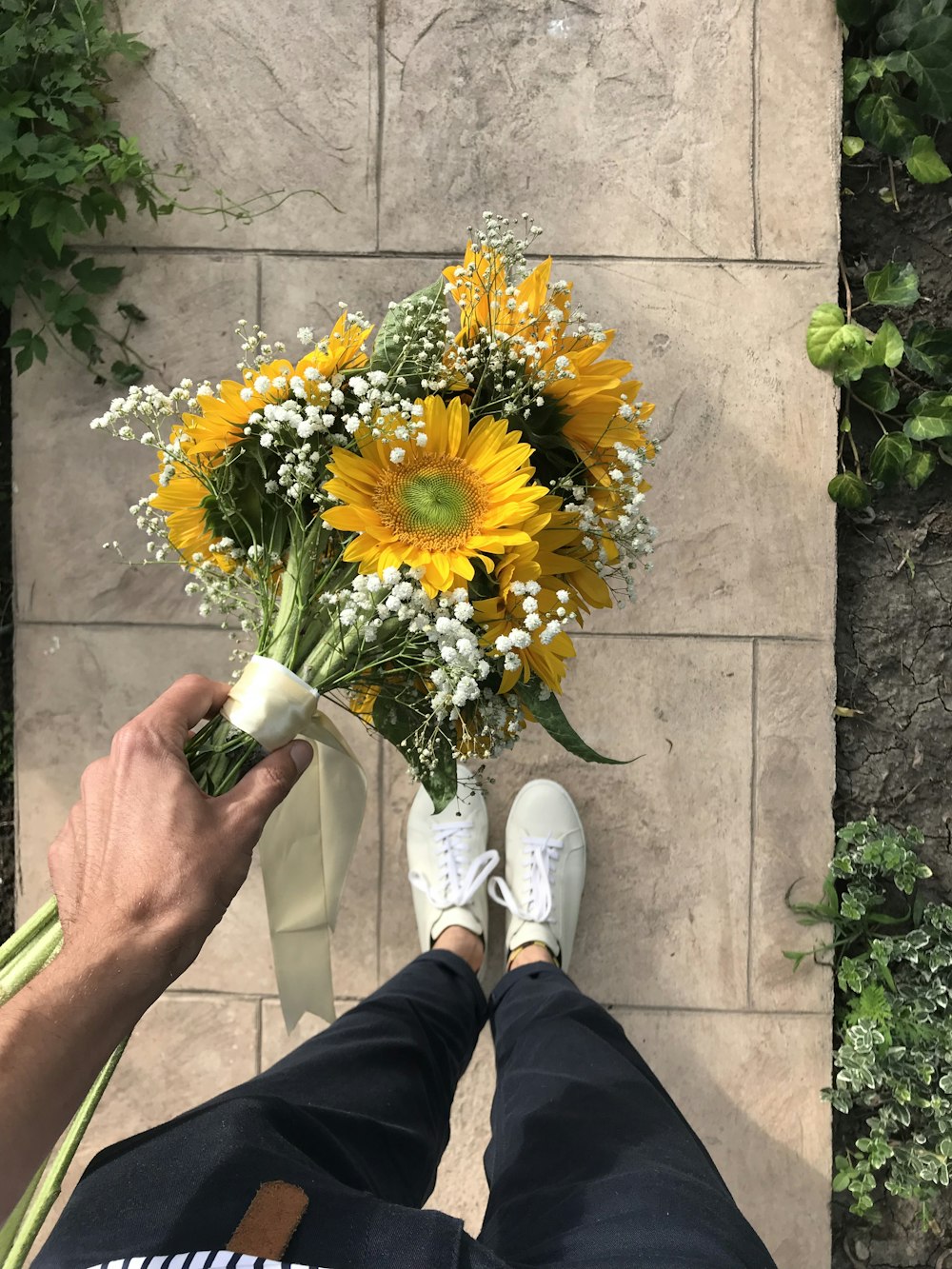 person in black pants and white shoes holding yellow sunflower bouquet