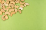 A cluster of cashew nuts scattered on a vibrant green surface, creating a contrast between the earthy tones of the nuts and the bright background.