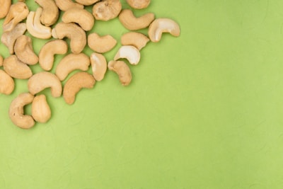 A cluster of cashew nuts scattered on a vibrant green surface, creating a contrast between the earthy tones of the nuts and the bright background.