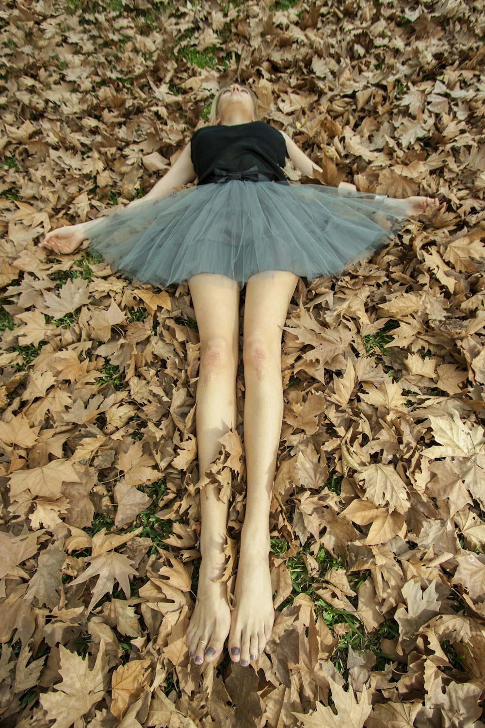 woman in black dress lying on dried leaves