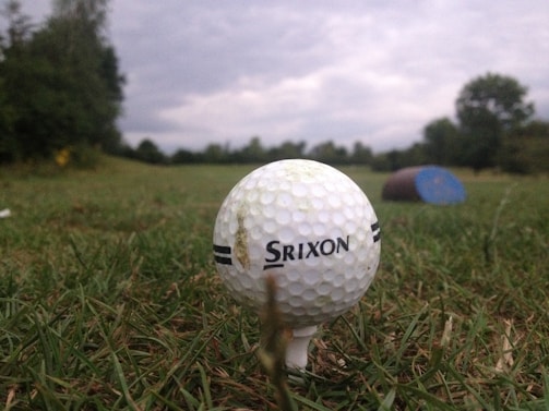 A close-up of a golf ball on a tee in a green field.
