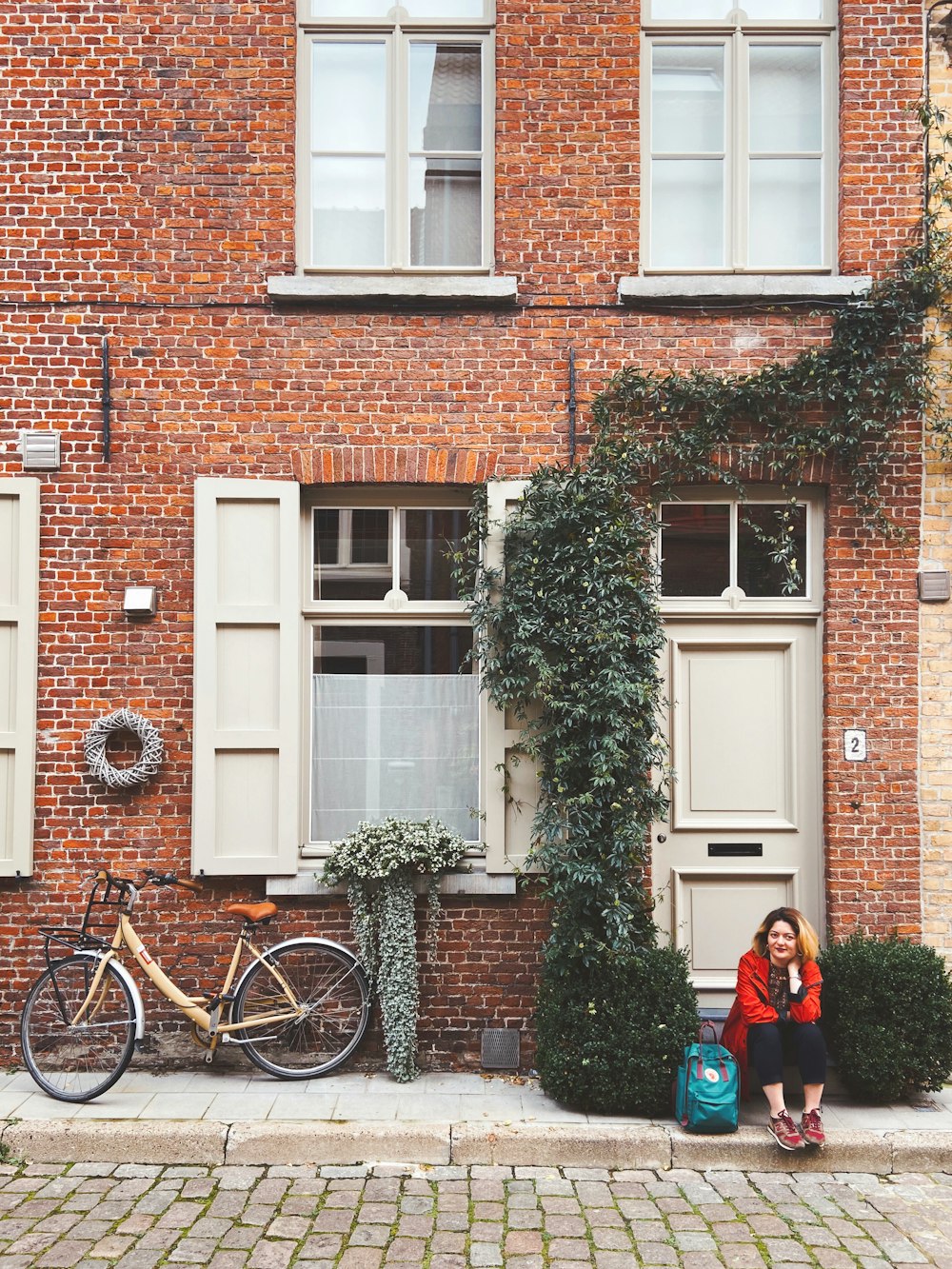 Frau in roter Jacke tagsüber neben braunem Backsteingebäude