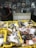 A man is standing in a shop, holding a smoking hookah pipe. In the foreground, yellow crates are filled with fresh fish, salmon steaks, and lobsters displayed on ice. The shop has a rustic appearance with various framed photos and a few appliances visible in the background.