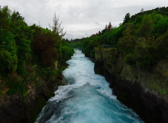 river between green trees under white clouds during daytime in Huka Falls New Zealand