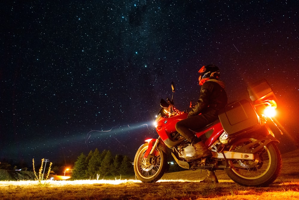 Hombre en traje de motocicleta rojo y negro que viaja en motocicleta roja bajo la noche estrellada