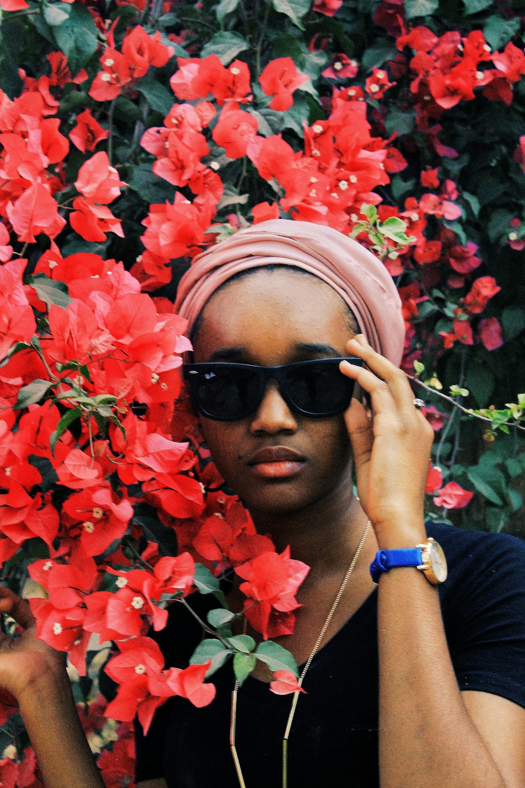 woman in black sunglasses and blue shirt holding red flowers