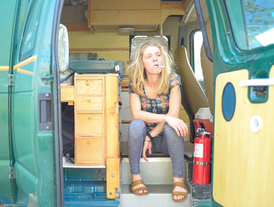 woman in blue denim shorts sitting on brown wooden box, Van life solo female van traveler brushing teeth inside van