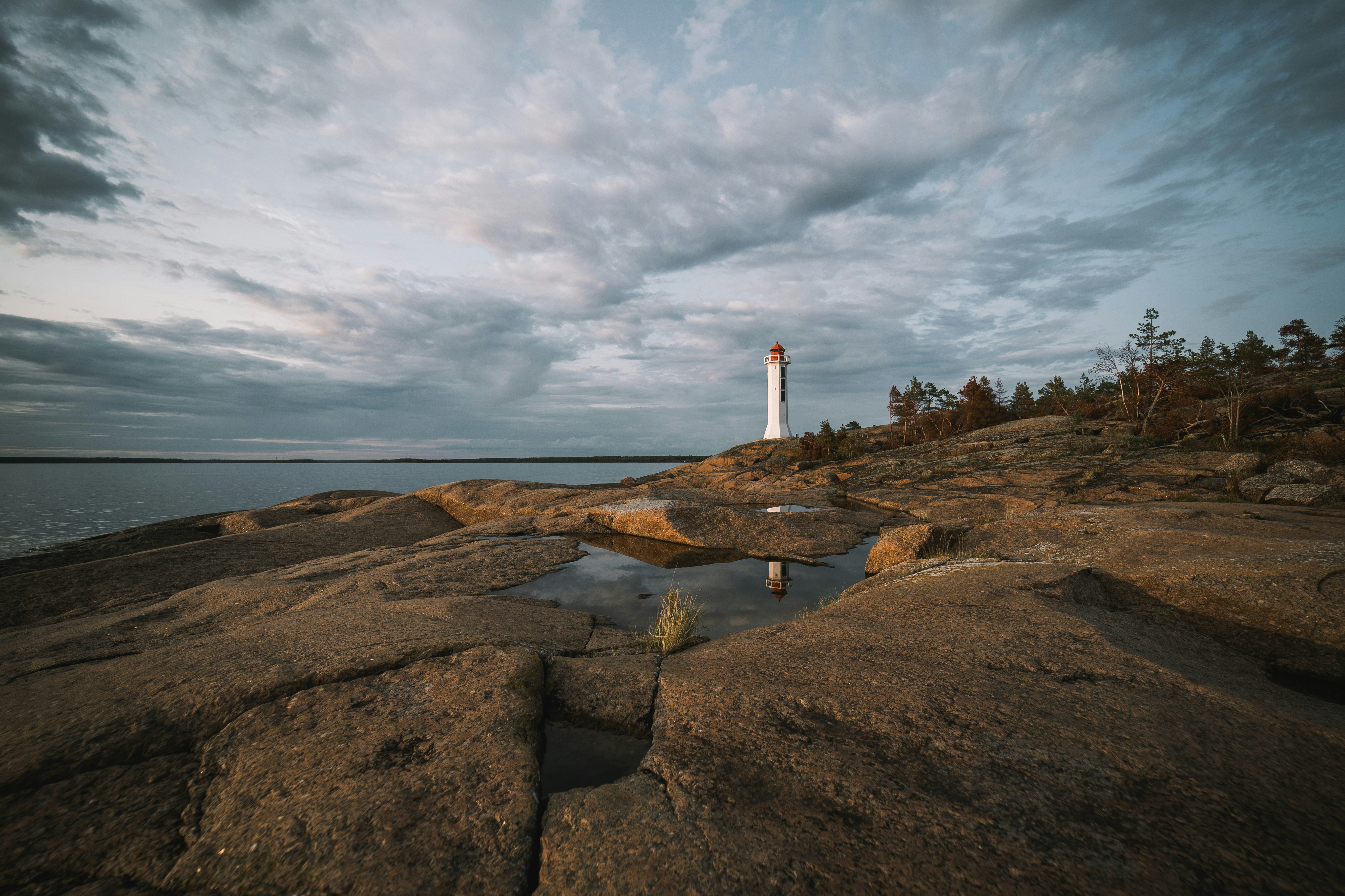 white and brown lighthouse on brown hill under white clouds and blue sky during daytime