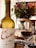 A bottle of Cune Rioja Crianza 2016 wine is placed prominently beside a filled wine glass. In the background, a cake decorated with marshmallows sits on a table covered with a decorative cloth. A colorful bouquet of roses and greenery adds a touch of elegance and vibrancy to the setting.