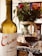 A bottle of Cune Rioja Crianza 2016 wine is placed prominently beside a filled wine glass. In the background, a cake decorated with marshmallows sits on a table covered with a decorative cloth. A colorful bouquet of roses and greenery adds a touch of elegance and vibrancy to the setting.