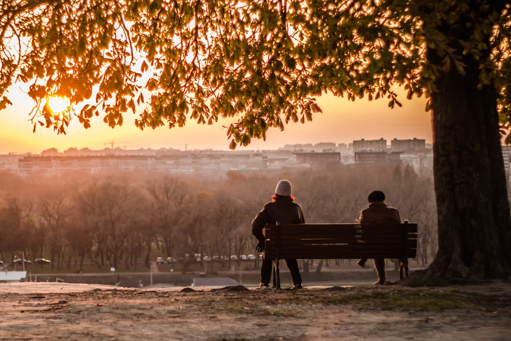 man and woman sitting on bench during sunset