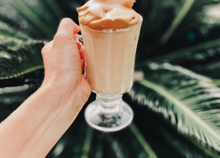 person holding clear glass cup with brown liquid