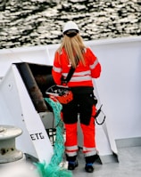 woman in orange jacket and white cap standing on boat during daytime