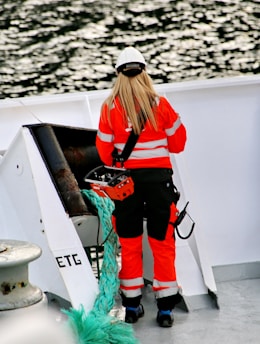 woman in orange jacket and white cap standing on boat during daytime