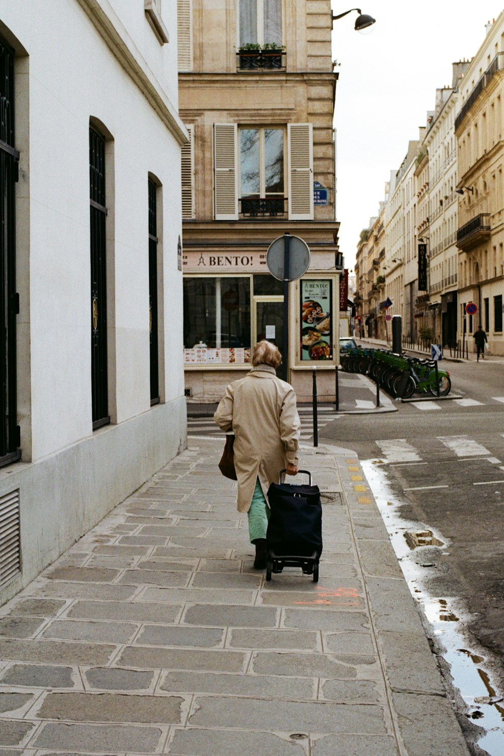 woman in beige coat sitting on sidewalk during daytime
