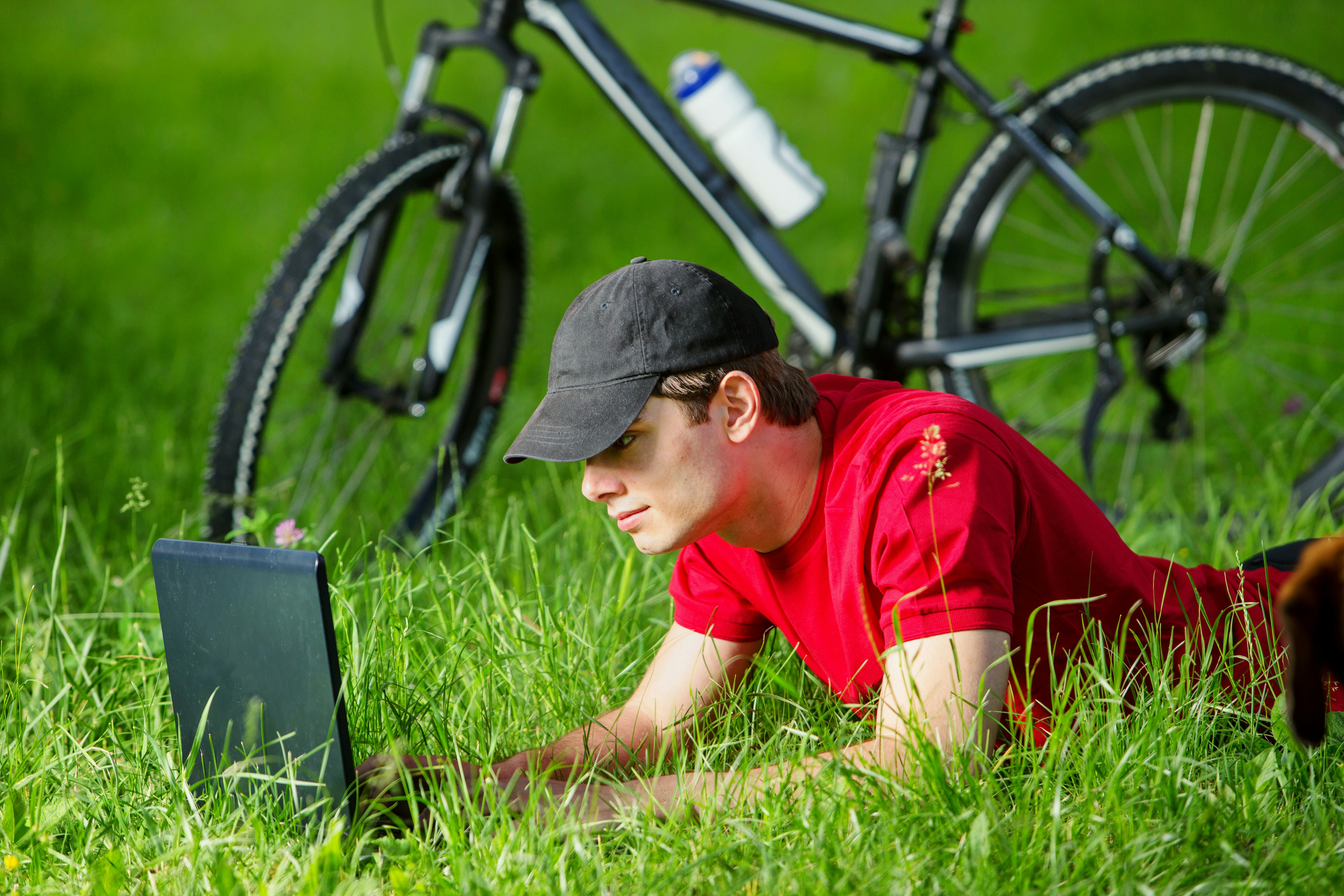 boy in red t-shirt and black cap sitting on green grass field