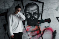 A model wearing a neutral-toned oversized sweatshirt standing against an urban graffiti wall.