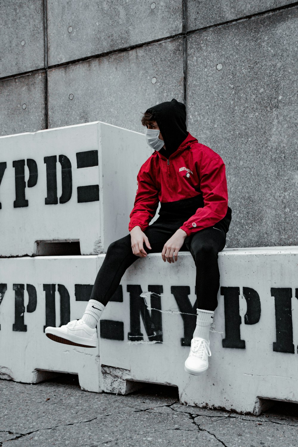 man in red jacket and black pants sitting on white and black no parking signage