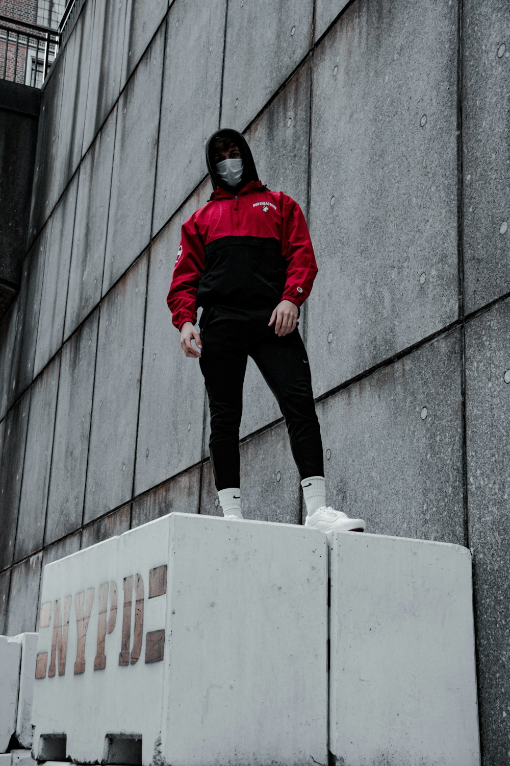 man in red jacket and black pants sitting on white concrete wall during daytime