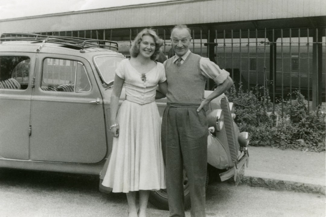 grayscale photo of 2 women standing beside car
