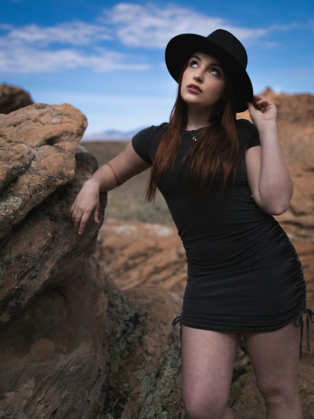 woman in black tank top and black shorts standing beside brown rock during daytime