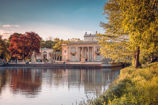 white concrete building near body of water during daytime in Łazienki Park Poland