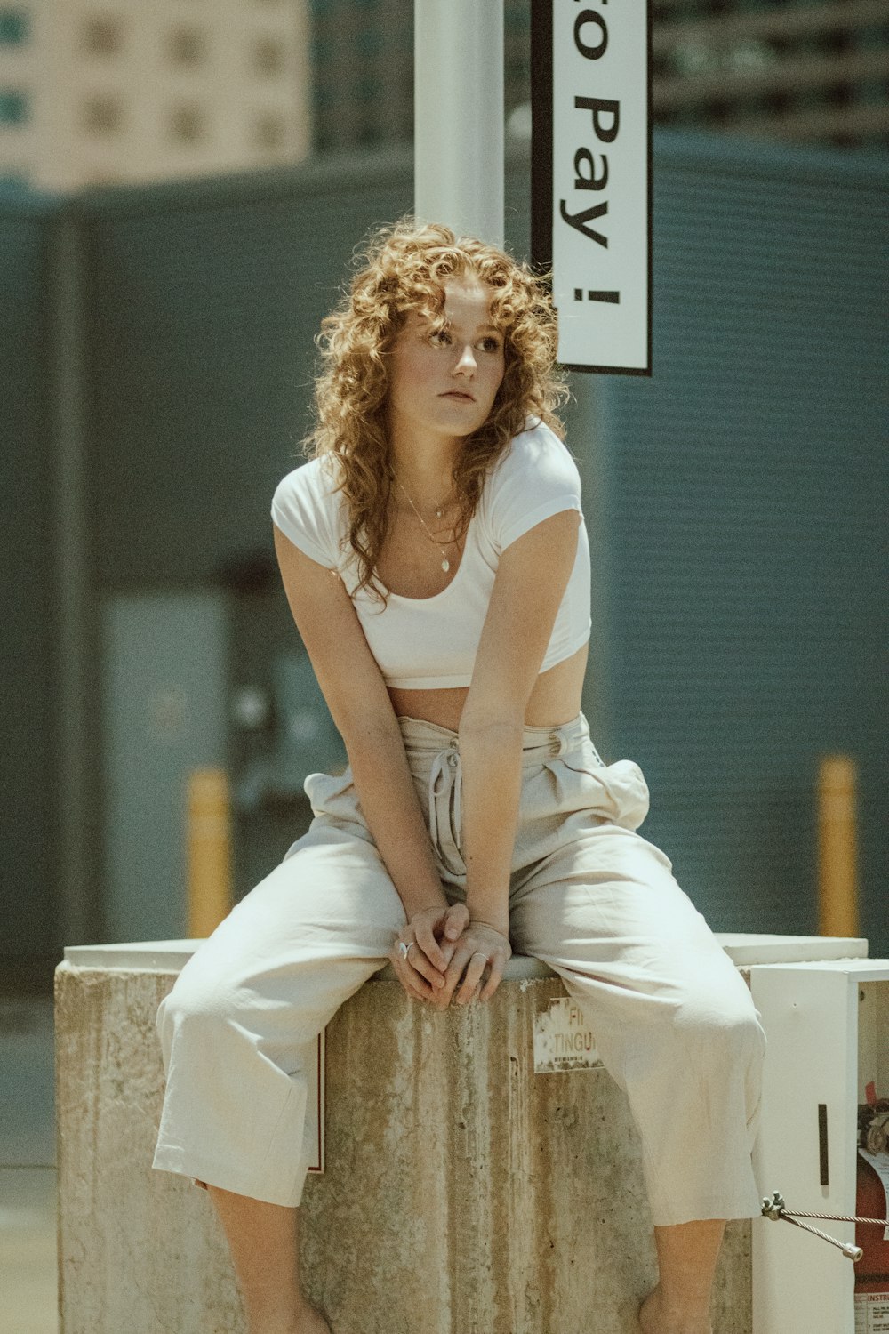 woman in white tank top and white pants sitting on white concrete bench