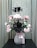 A floral arrangement with pink and black flowers in a clear vase filled with decorative crystals, adorned with a pink ribbon. The background features a neutral curtain, providing a soft backdrop for the vibrant flowers.