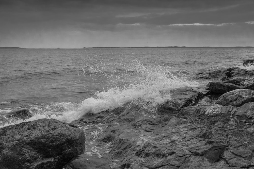 Foto in scala di grigi delle onde dell'oceano che si infrangono sulle rocce
