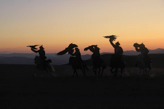A group of riders crossing a wide open steppe with distant mountains glowing in the late afternoon light.