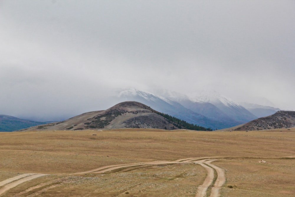 brown field near mountain under white clouds during daytime