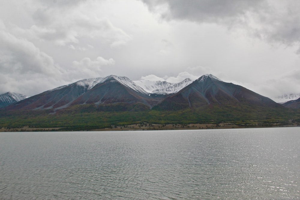 green and brown mountain near body of water under white clouds during daytime