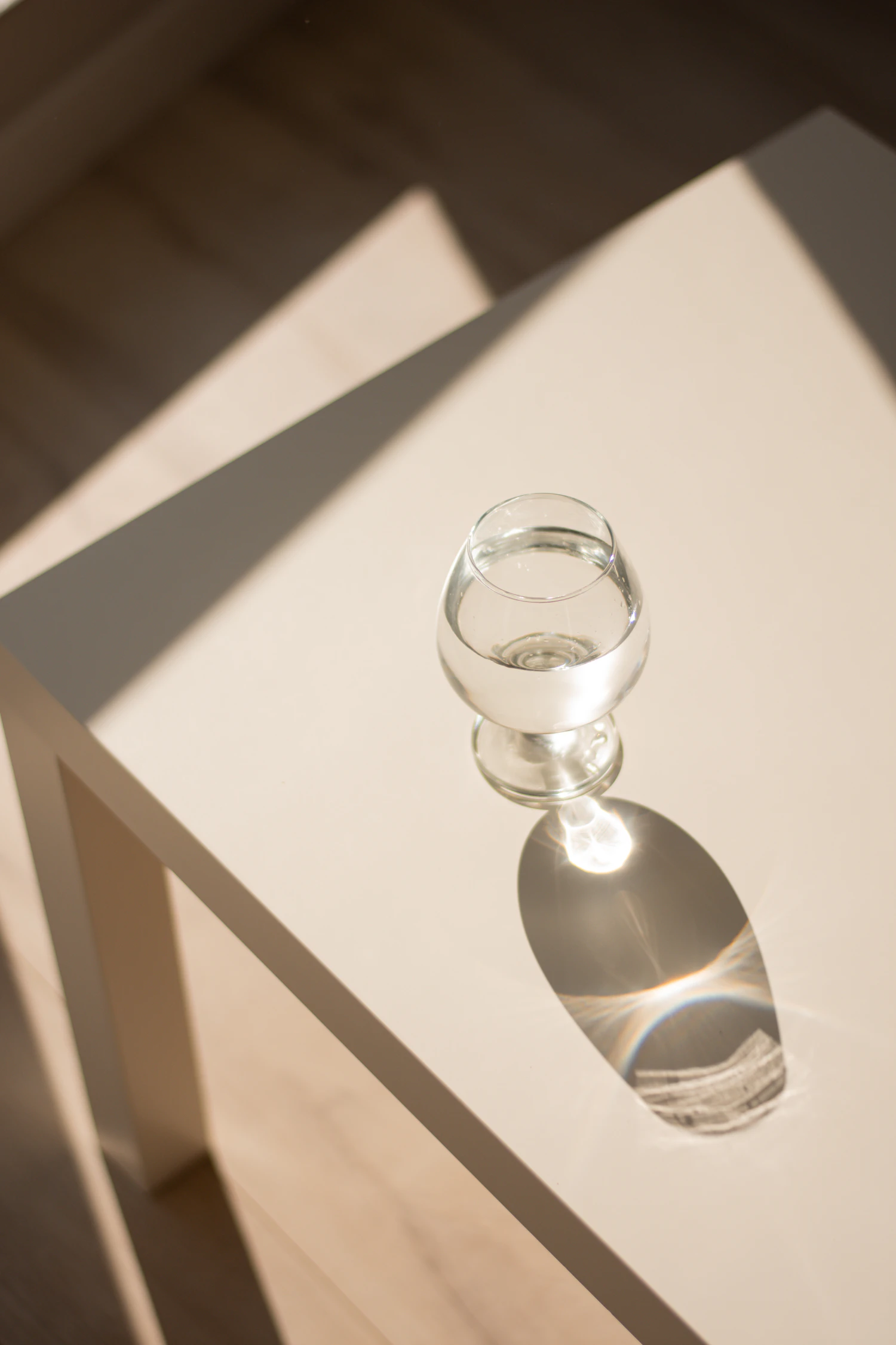 A small footed cordial glass in a shaft of sun, its shadow bright with light