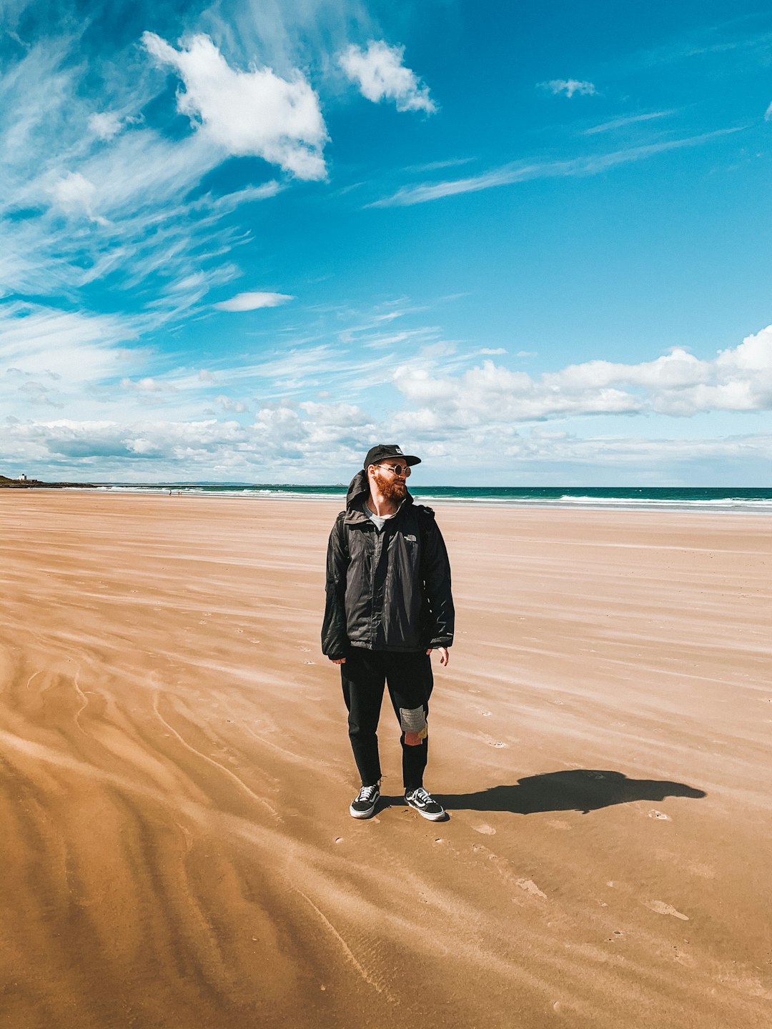 woman in black coat standing on brown sand near sea during daytime