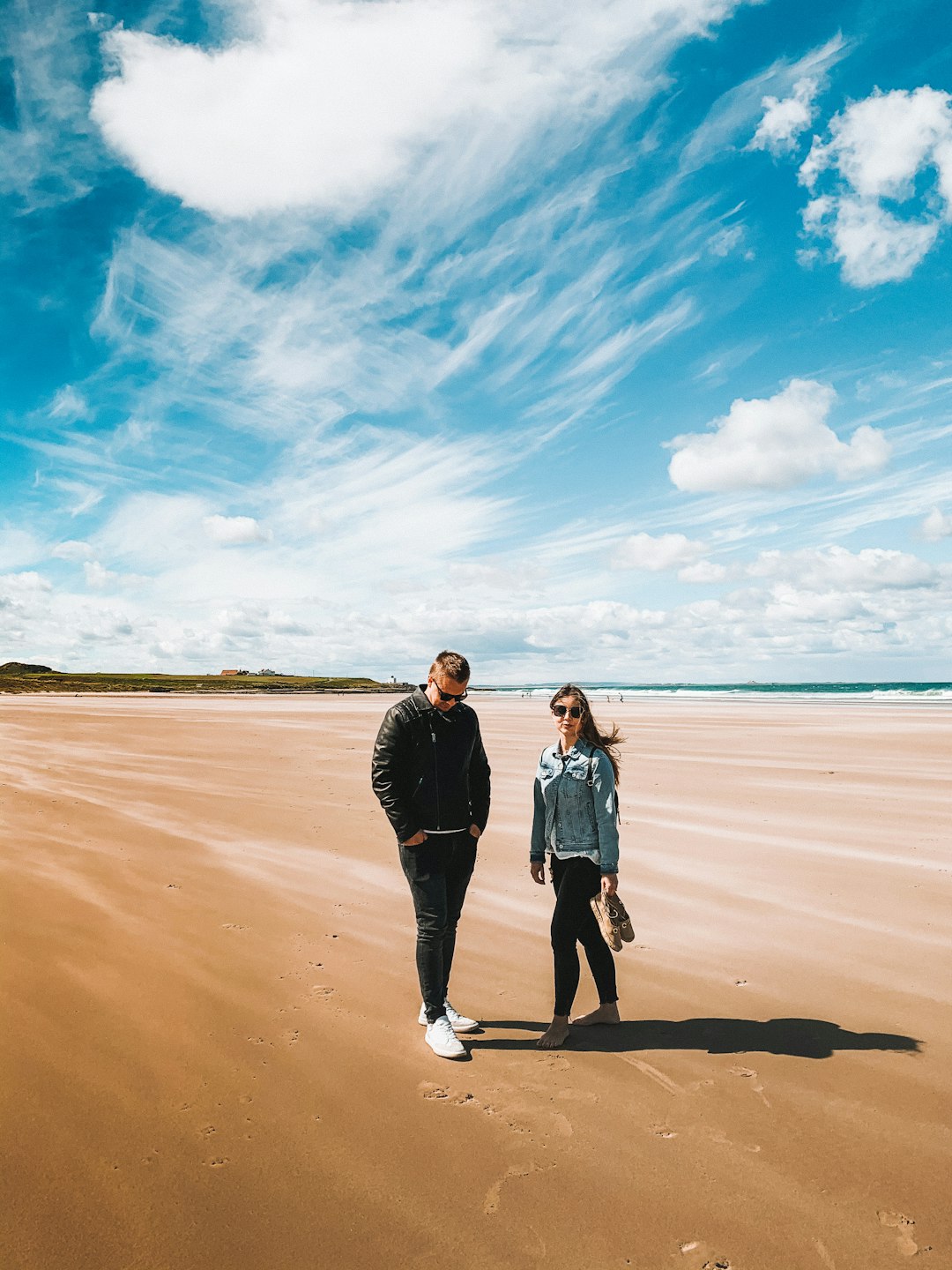 man and woman standing on brown sand near body of water during daytime