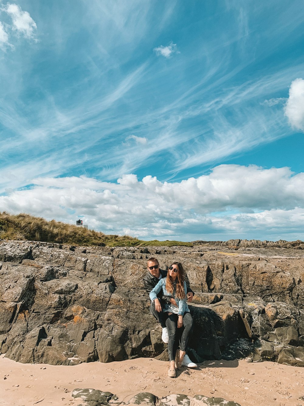 woman in white tank top and blue denim shorts standing on brown rock formation under blue