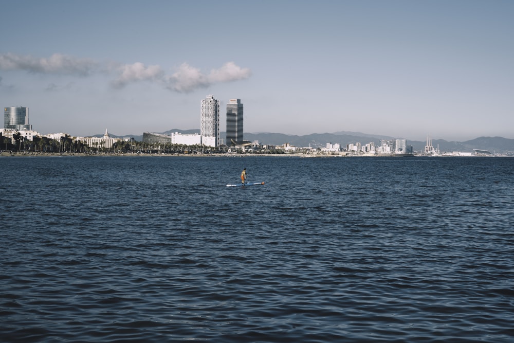 people swimming on sea near city buildings during daytime