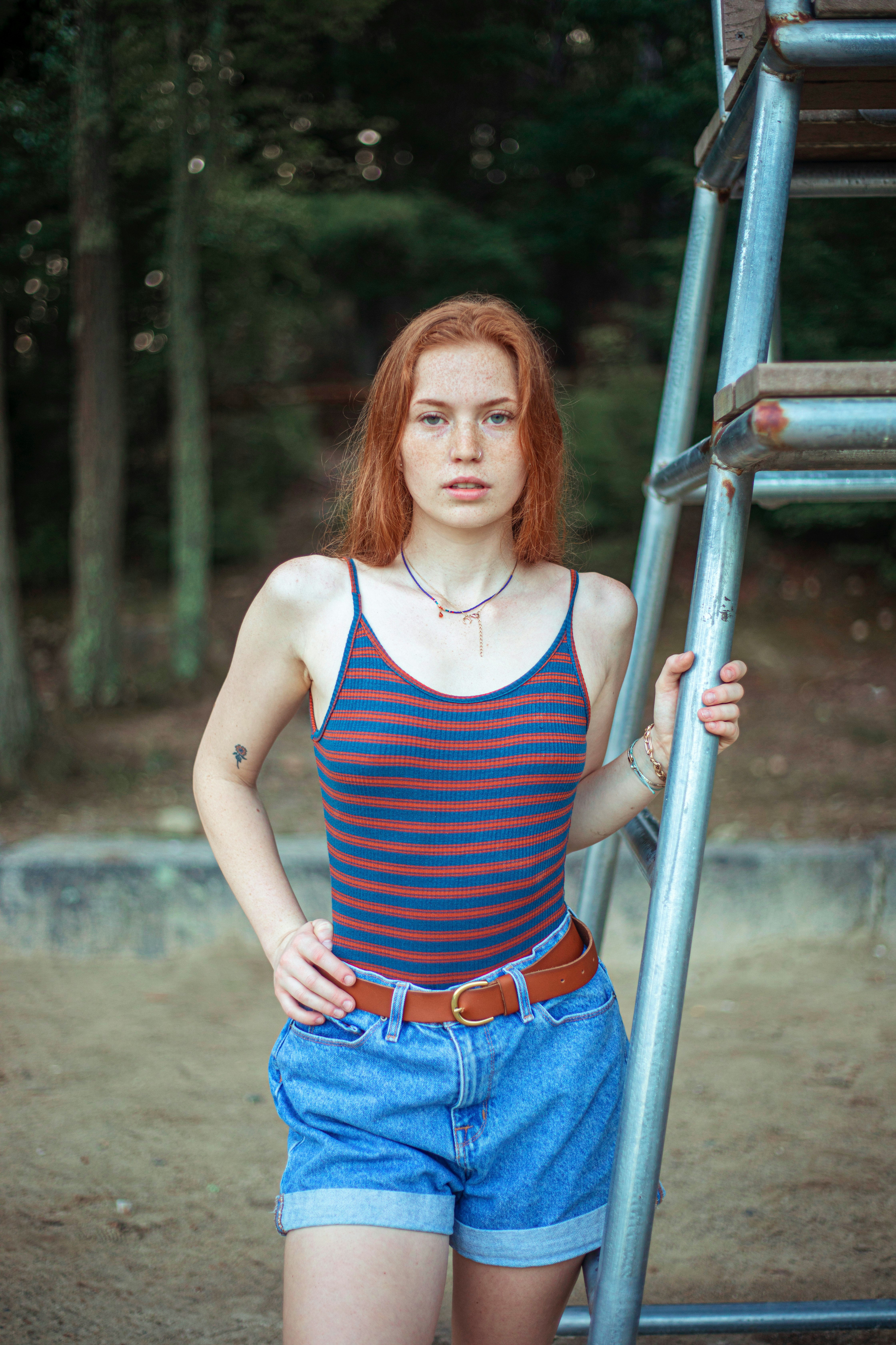 woman in blue and white stripe tank top and blue denim jeans standing beside gray metal